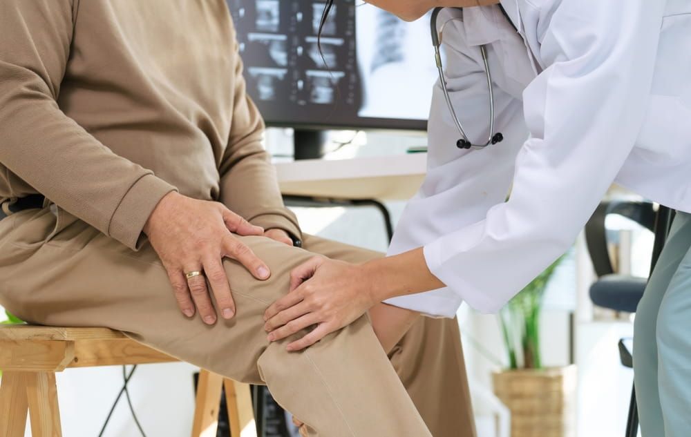 Doctor examining senior patient for osteoarthritis and knee pain during orthopedic checkup in hospital